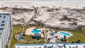 Vue aérienne d’un complexe hôtelier en bord de mer, avec une piscine, des chaises longues et un bâtiment surmonté d’une piscine sur le toit.