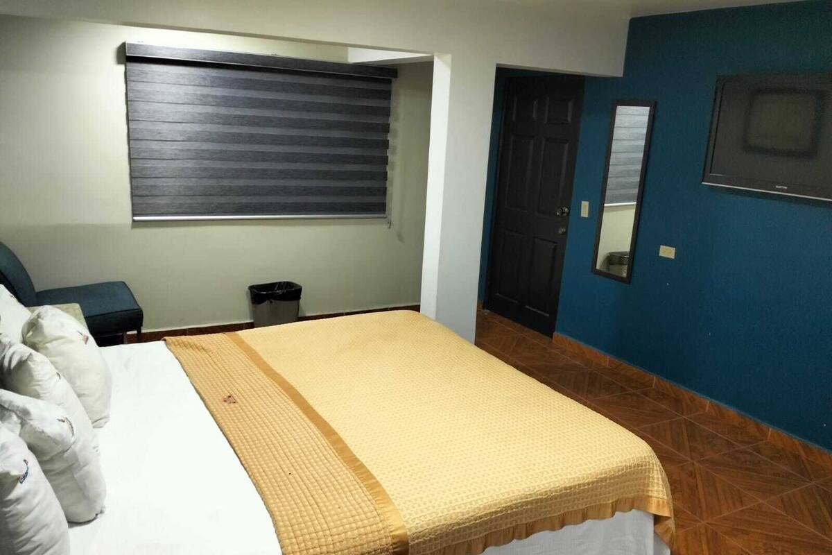 Ein Schlafzimmer mit einem Bett, einem Fenster mit Jalousien, einer Tür und einem Spiegel an der Wand.
