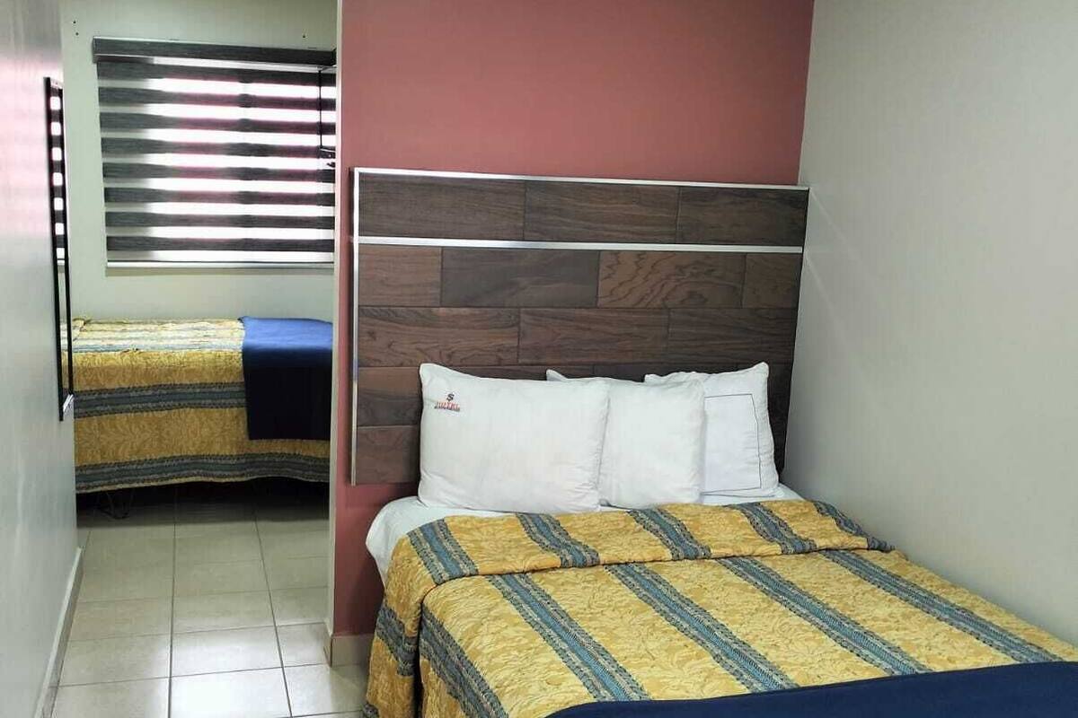 Ein Hotelzimmer mit zwei Betten, einem Holzkopfstück und einem Fenster mit Jalousien.