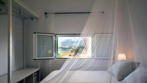 Un dormitorio con cama, ventana y vista al mar.