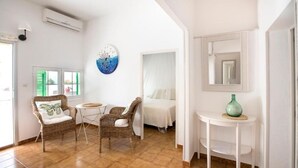 Una habitación con una cama, dos sillones de mimbre, una mesita, un espejo y una obra de arte en la pared.