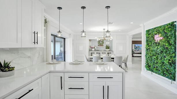 A modern kitchen with white cabinetry, pendant lighting, and a green vertical garden wall.