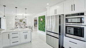 A modern kitchen with white cabinetry, stainless steel appliances, and pendant lighting.