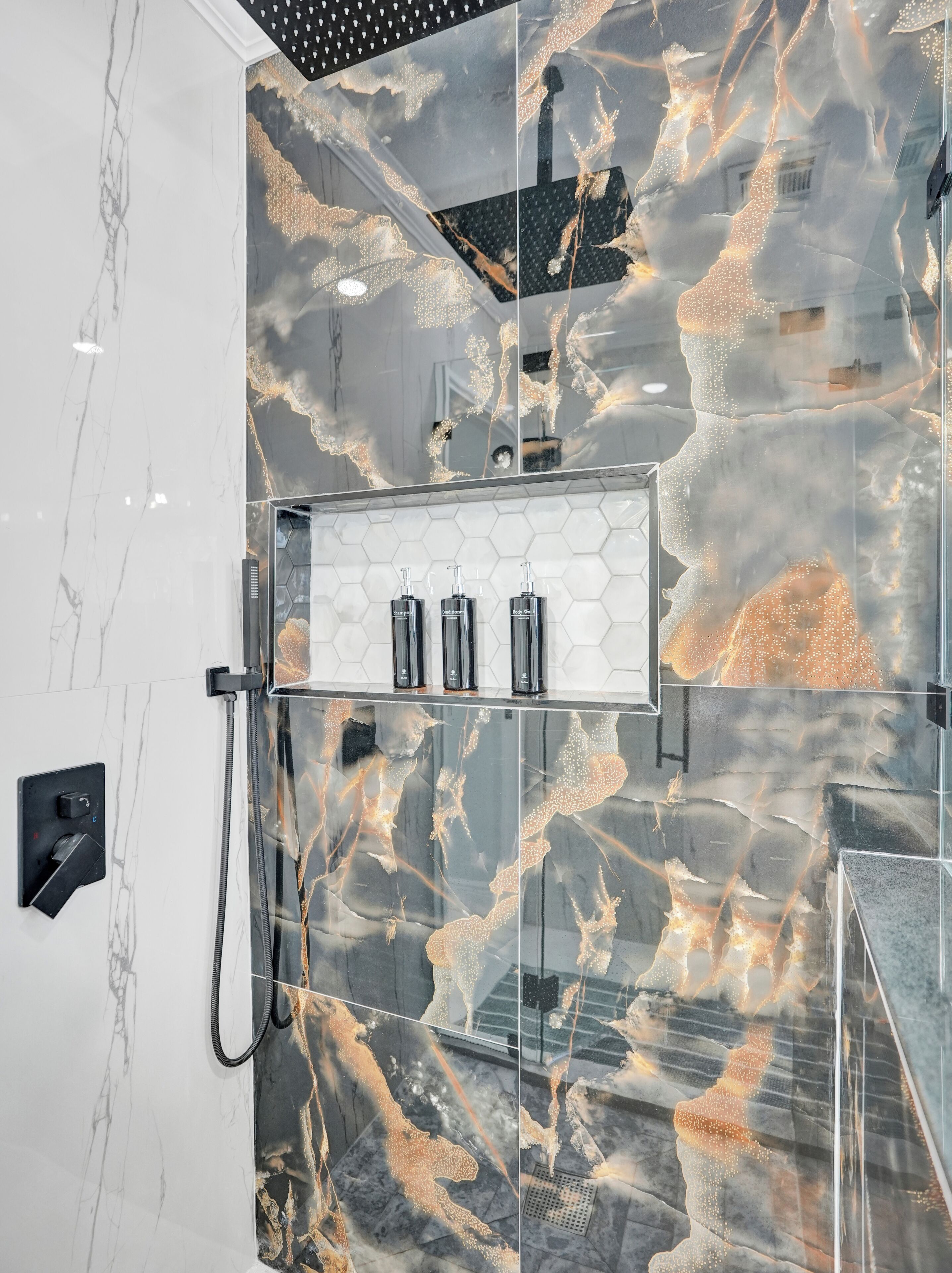 A modern bathroom with a marble shower wall, a glass-enclosed shower, and a built-in soap dispenser shelf.