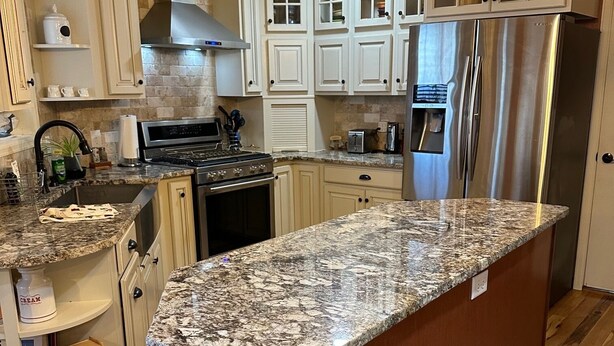 A kitchen with white cabinets, a granite countertop, stainless steel appliances, and a wooden floor.