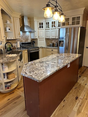 A kitchen with white cabinets, a granite countertop, stainless steel appliances, and a wooden floor.