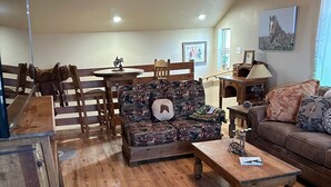 A cozy living room with wooden furniture, a sofa with a horse-themed cushion, and a dining area with a wooden table and chairs.