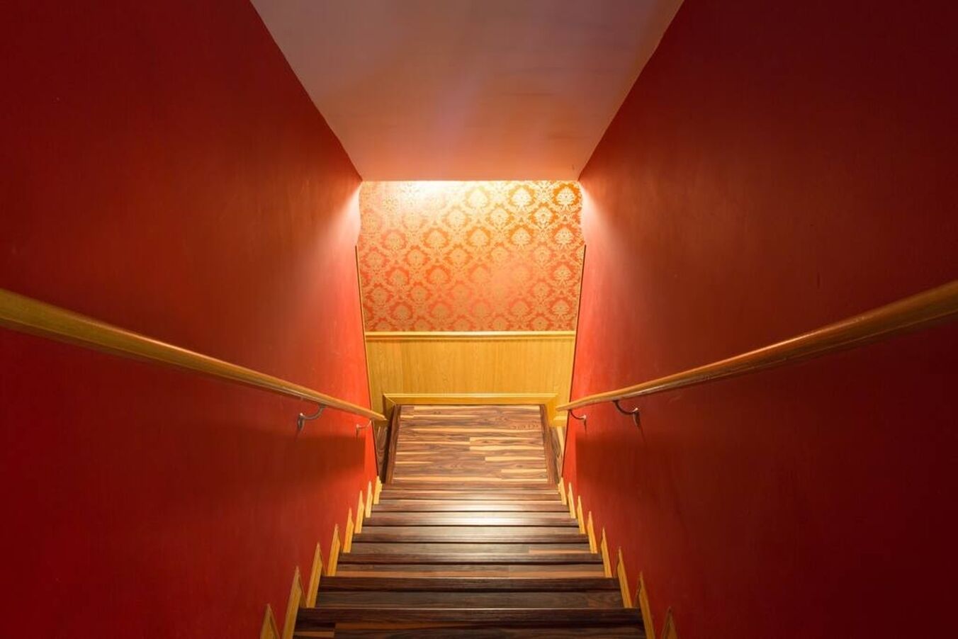 A staircase with wooden steps and yellow handrails, leading to a landing with patterned wallpaper.