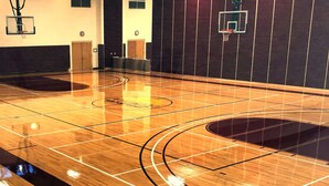 Una cancha de baloncesto interior con suelo de madera, aro de baloncesto y marcador.
