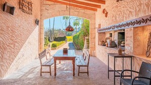 An outdoor dining area with a stone archway, wooden benches, a table, and a hanging light fixture. - Villa es Rafal by Mallorca North Villas  (Santa Margalida)