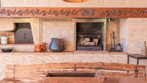 A rustic kitchen with a brick fireplace, wooden shelves, and a stone countertop. - Villa es Rafal by Mallorca North Villas  (Santa Margalida)