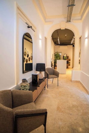 A modern interior with a sofa, a lamp, a mirror, and a dining area in the background.