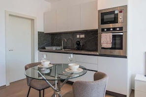 A modern kitchen with white cabinets, a glass dining table, and stainless steel appliances.