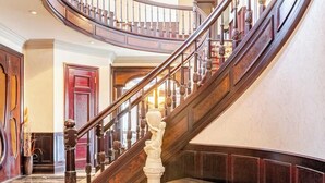 Un magnifique escalier à volutes, orné d’un lustre, de rampes en bois et d’une statue à sa base.