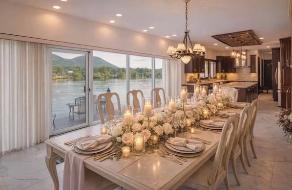 A dining area with a long table set for a meal, a chandelier, and a view of a lake.