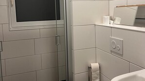 A bathroom with a toilet, a sink, a mirror, and a shower enclosure. - NR 6 ground floor 3 ZKB for families and companies (Fuldatal)