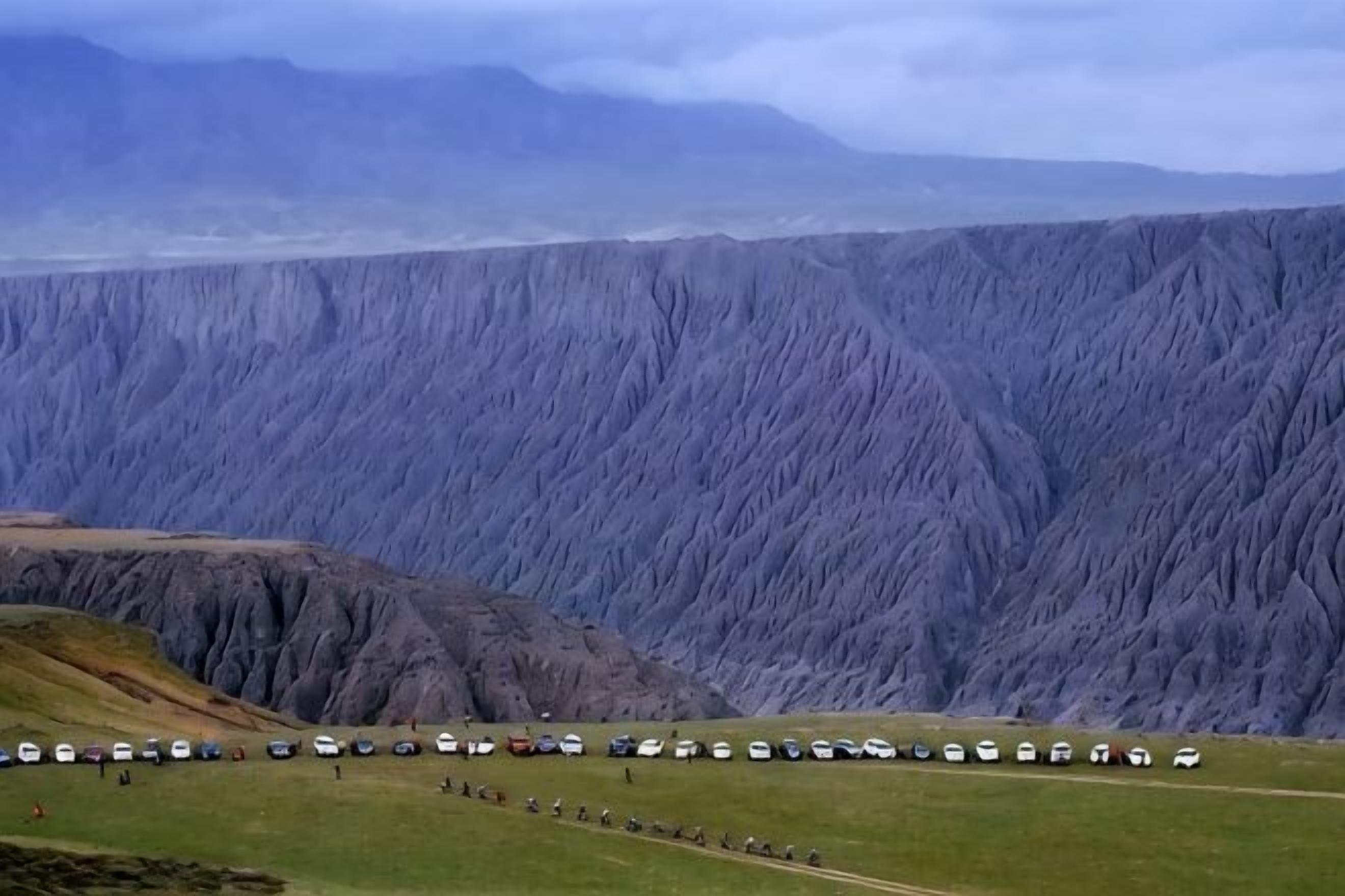 A mountainous landscape with a row of vehicles parked on a flat area.