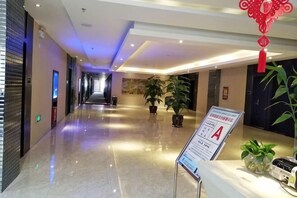Un pasillo de hotel con piso pulido, plantas en macetas, un mostrador de recepción y un cartel.