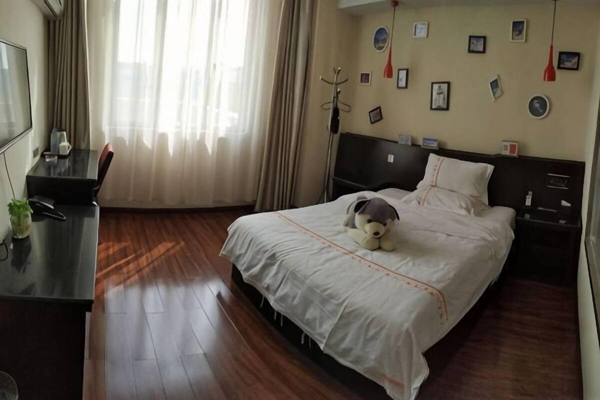 A hotel room with a bed, a desk, a chair, a TV, and a window with curtains.