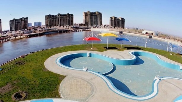 A waterfront park with a winding pool, umbrellas, and a view of the city skyline. - Lemon Hotel (Karamay Dushanzi) (Karamay)