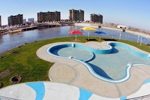 A waterfront park with a winding pool, umbrellas, and a view of the city skyline.