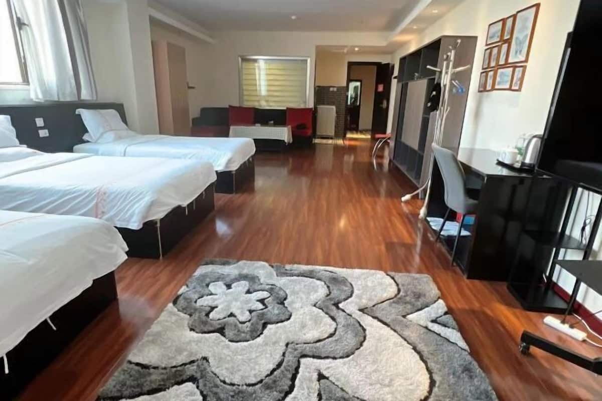 A hotel room with two beds, a desk, a chair, a TV, and a bathroom visible in the background.