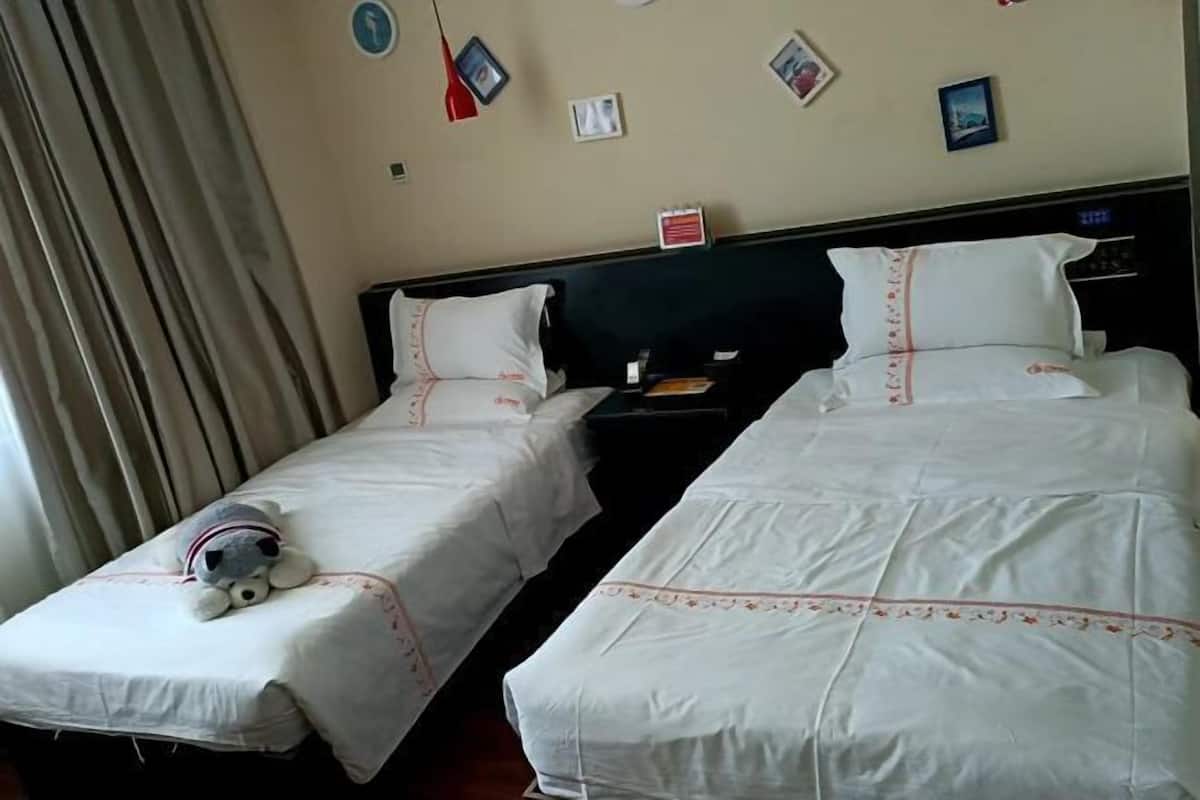 A hotel room with two beds, a nightstand, and a teddy bear on one bed.