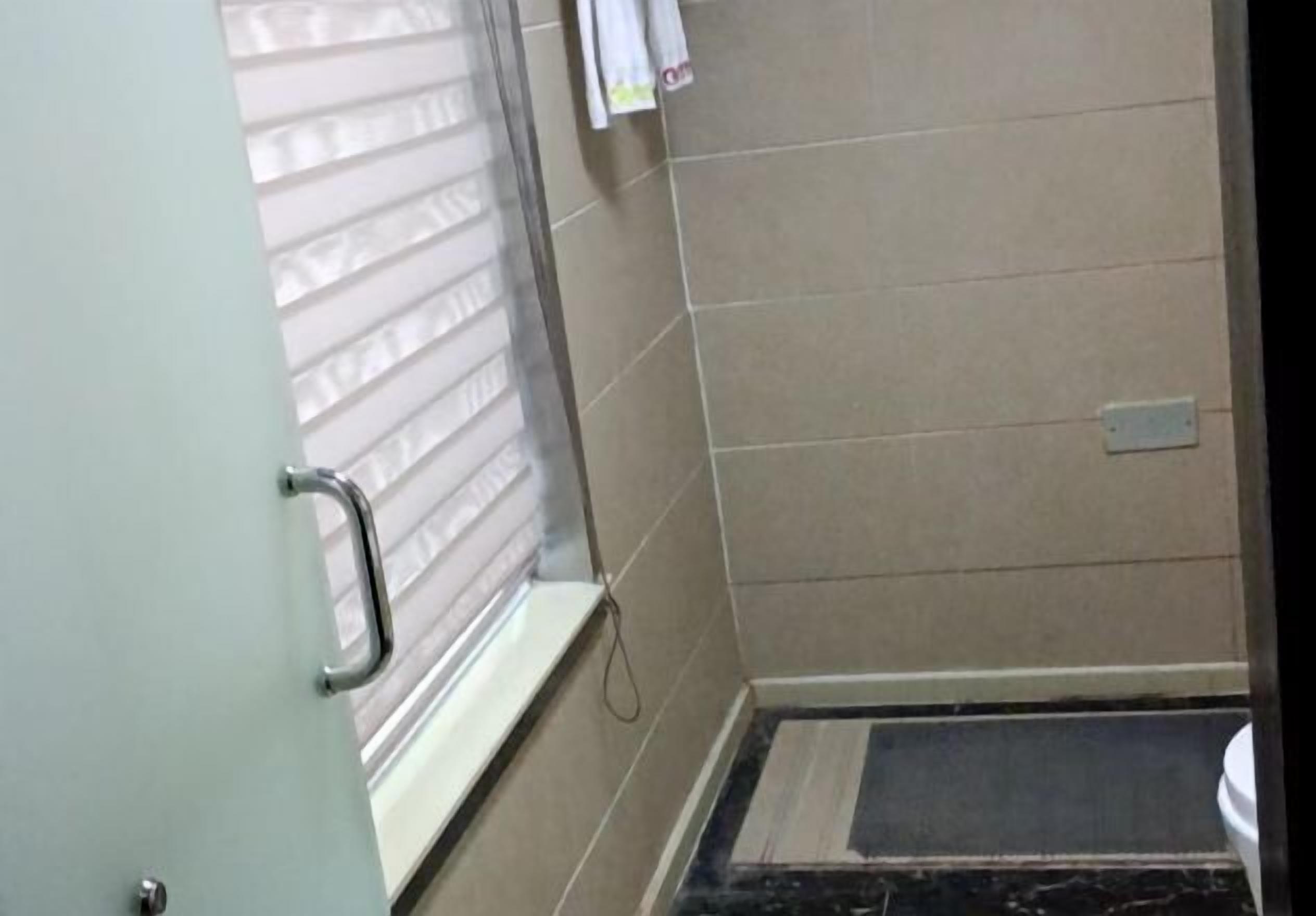 A bathroom with a shower, a window with blinds, and a tiled floor.
