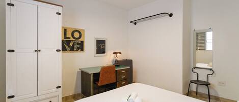 A hotel room with a bed, a desk, a wardrobe, a mirror, and a ceiling fan.