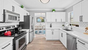 Una cocina moderna con muebles blancos, electrodomésticos de acero inoxidable y una isla central.
