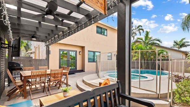 Un patio cubierto con piscina, muebles de madera y vista a una casa.