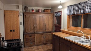 Une cuisine avec des meubles de rangement en bois, une cuisinière, un évier et une fenêtre ornée de rideaux à carreaux.