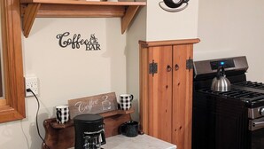 Une cuisine équipée d’un espace dédié au café, d’étagères remplies d’ustensiles de cuisine, d’une cuisinière et d’une bouilloire fixée au mur.