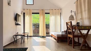 A room with a bed, a desk, a chair, a TV, and a view of greenery outside.