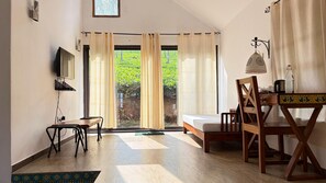 A room with a bed, a desk, a chair, a TV, and a view of greenery outside. - Tea Terrace Vythiri Resort (Vythiri)