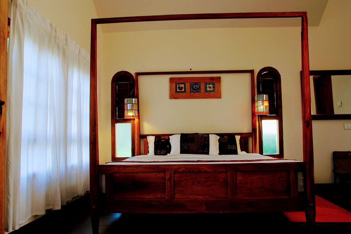 Una cama con dosel de madera, ropa de cama blanca y dos lámparas fijadas a la pared.