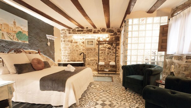 A bedroom with a bed, a sitting area with a sofa, a bathtub, and a stone wall. - Lo Raconet dárnes, a rural apartment in the historical center of Arnes. (Arnes)