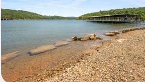 Un lago tranquillo con un molo di legno che si protende sull'acqua, circondato da terreno roccioso e dolci colline verdi.