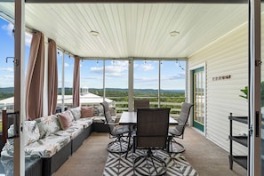 A covered patio with a table and chairs, a sofa with cushions, and a view of the landscape. - Completely Remodeled Table Rock Retreat: Cozy Lake View Condo + Screened Porch (Kimberling City)