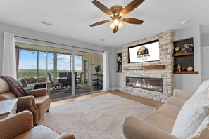 A spacious living room with a fireplace, a ceiling fan, and a large sliding glass door leading to an outdoor patio. - Completely Remodeled Table Rock Retreat: Cozy Lake View Condo + Screened Porch (Kimberling City)