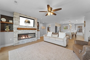 A living room with a stone fireplace, a ceiling fan, a white sofa, and a kitchen in the background. - Completely Remodeled Table Rock Retreat: Cozy Lake View Condo + Screened Porch (Kimberling City)