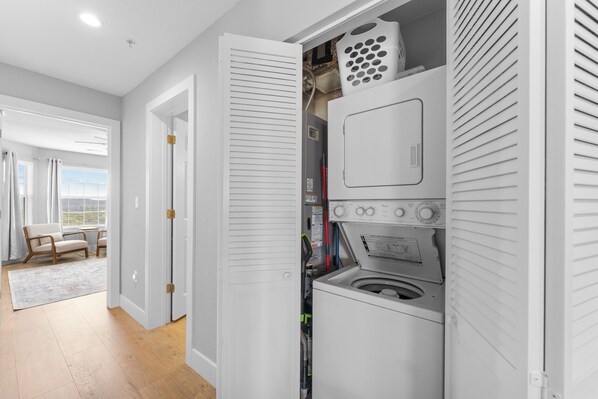A laundry room with a washing machine and dryer, a window with curtains, and a chair in the adjacent room. - Completely Remodeled Table Rock Retreat: Cozy Lake View Condo + Screened Porch (Kimberling City)