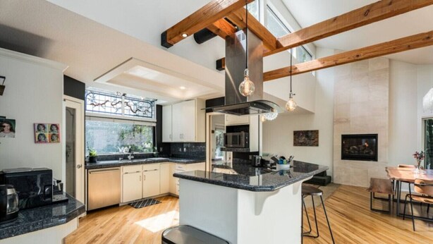 A modern kitchen with a central island, wooden beams, and a dining area with a table and chairs. - Treetop Castle *Sleeps 16* (Boise)