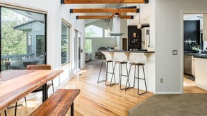 A modern kitchen with wooden beams, a dining area with a wooden table and benches, and a view of the outdoors. - Treetop Castle *Sleeps 16* (Boise)