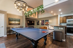 A spacious living area with a ping pong table, a kitchen with wooden cabinets, and a hanging plant. - Treetop Castle *Sleeps 16* (Boise)