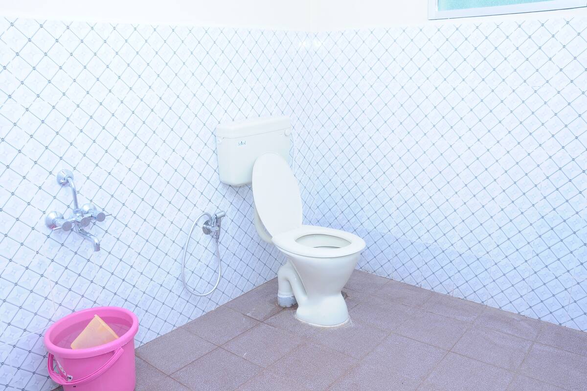 A bathroom with a white toilet, a pink bucket, and a shower area.