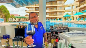 Een man houdt een wijnglas vast bij een poolbar, met uitzicht op een hotelzwembad en ligstoelen.