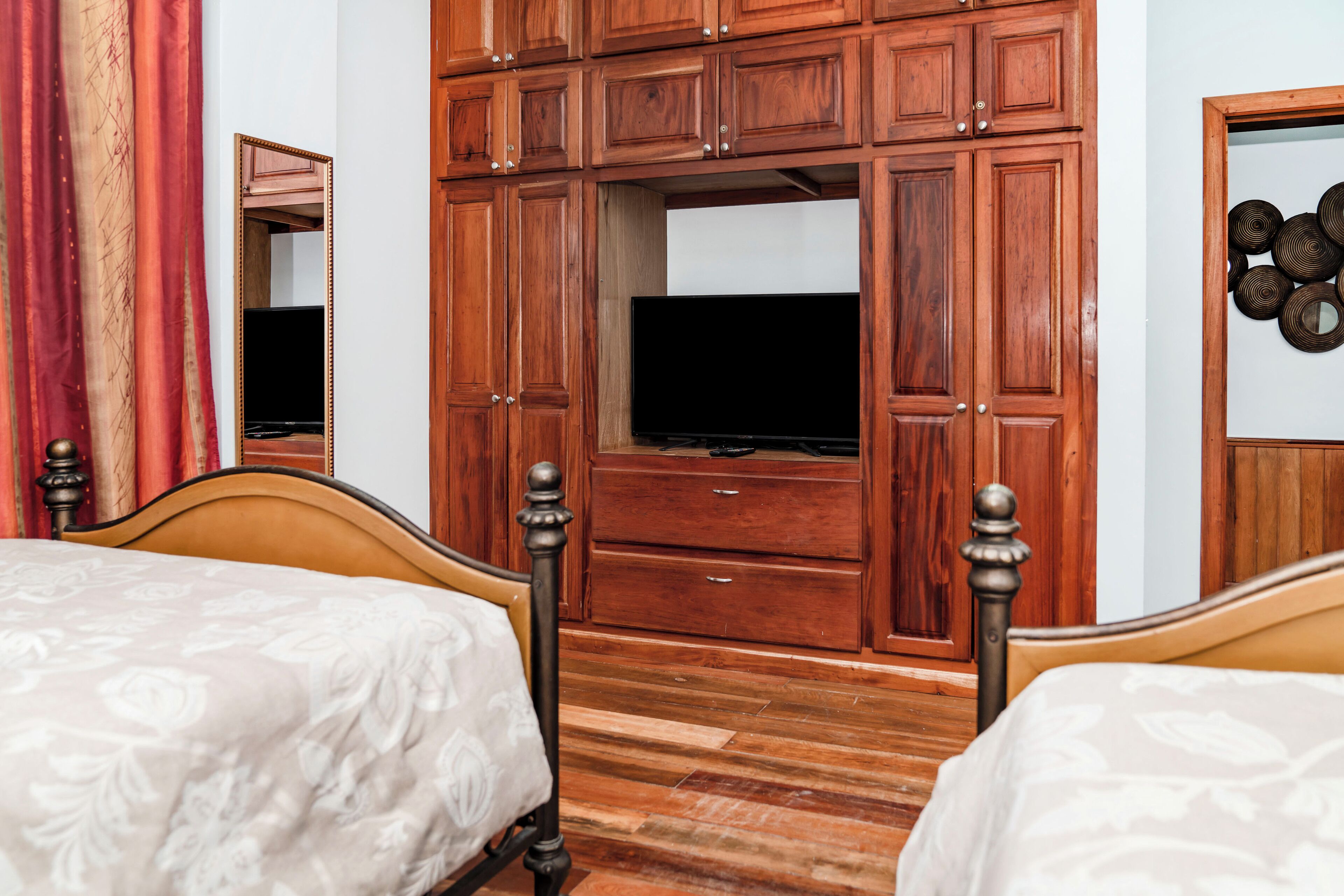 Ein Schlafzimmer mit zwei Betten, einem Holzschrank, einem Fernseher und einem Spiegel.