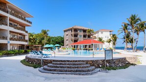 A resort with a swimming pool, lounge chairs, and a beach area. - Luxury Beachfront Condo - Condo 17 at Oceans 23, Belize (San Pedro)