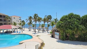 Une piscine d’un complexe hôtelier, bordée de pierres, agrémentée de palmiers et dotée d’un espace plage.